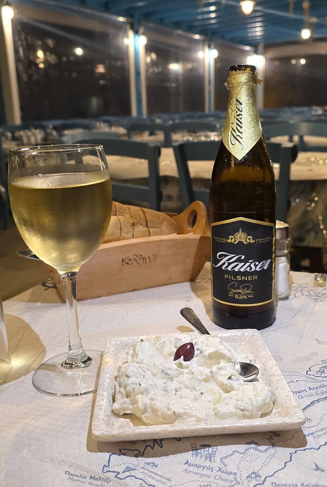 Tzatziki maison, pain et boissons locales sur une table nappée de la carte d'Amorgos au restaurant Korali, Aegiali, Amorgos
