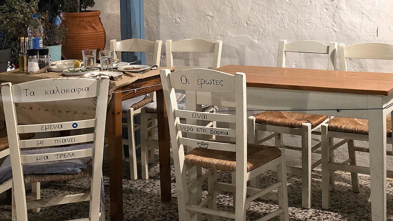 Chaises en bois peintes de vers grecs et table dressée dans la taverne familiale Parvas, Chora d'Amorgos