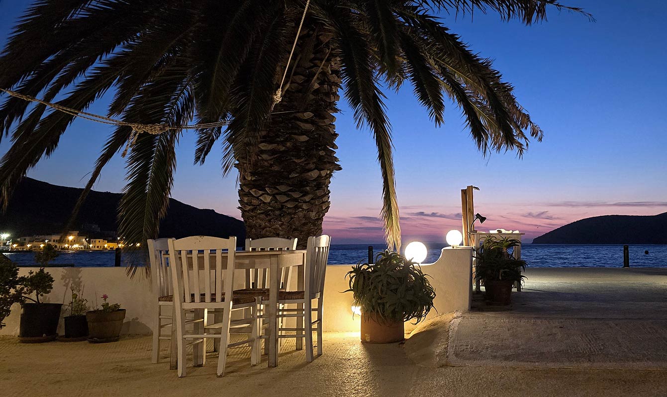 Terrasse d'Anemi au bord de l'eau au crépuscule, tables blanches sous les palmiers face à la mer, Katapola, Amorgos