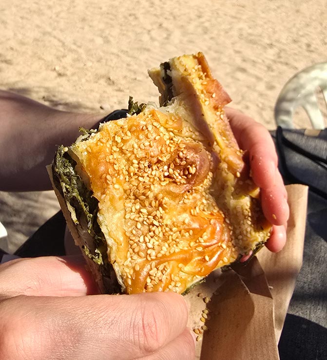 Part de tourte aux herbes dorée au sésame dégustée sur la plage de Kalotaritissa, Amorgos