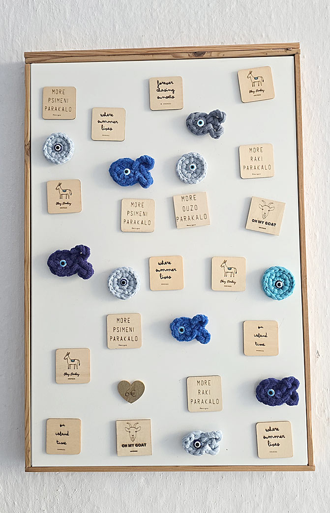 Les aimants et petites plaques en bois gravées : messages malicieux et 100 % Amorgos comme « More psiméni parakaló », « More raki parakaló », « On my goat » ou « Where summer lives ».