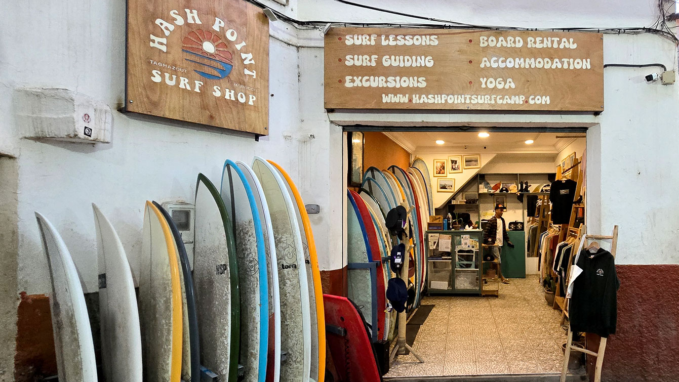 Devanture du Hash Point Surf Shop à Taghazout, planches de surf alignées le long du mur.la piste en quad, direction le canyon