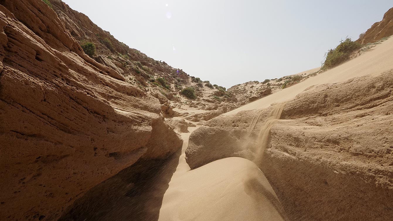Sortie du canyon de Timlalin, sable s'écoulant sur la pente et végétation en surplomb.