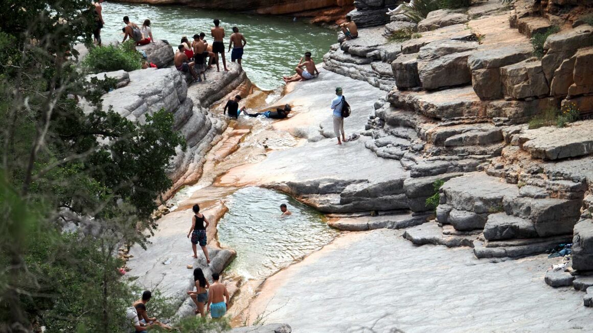Vasque isolée vue depuis le sentier en hauteur, un baigneur assis sur la dalle Vallée du Paradis, Agadir