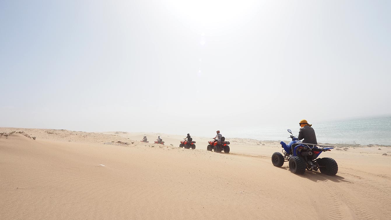 File de quads sur une piste de sable vers l'océan aux dunes de Timlalin.