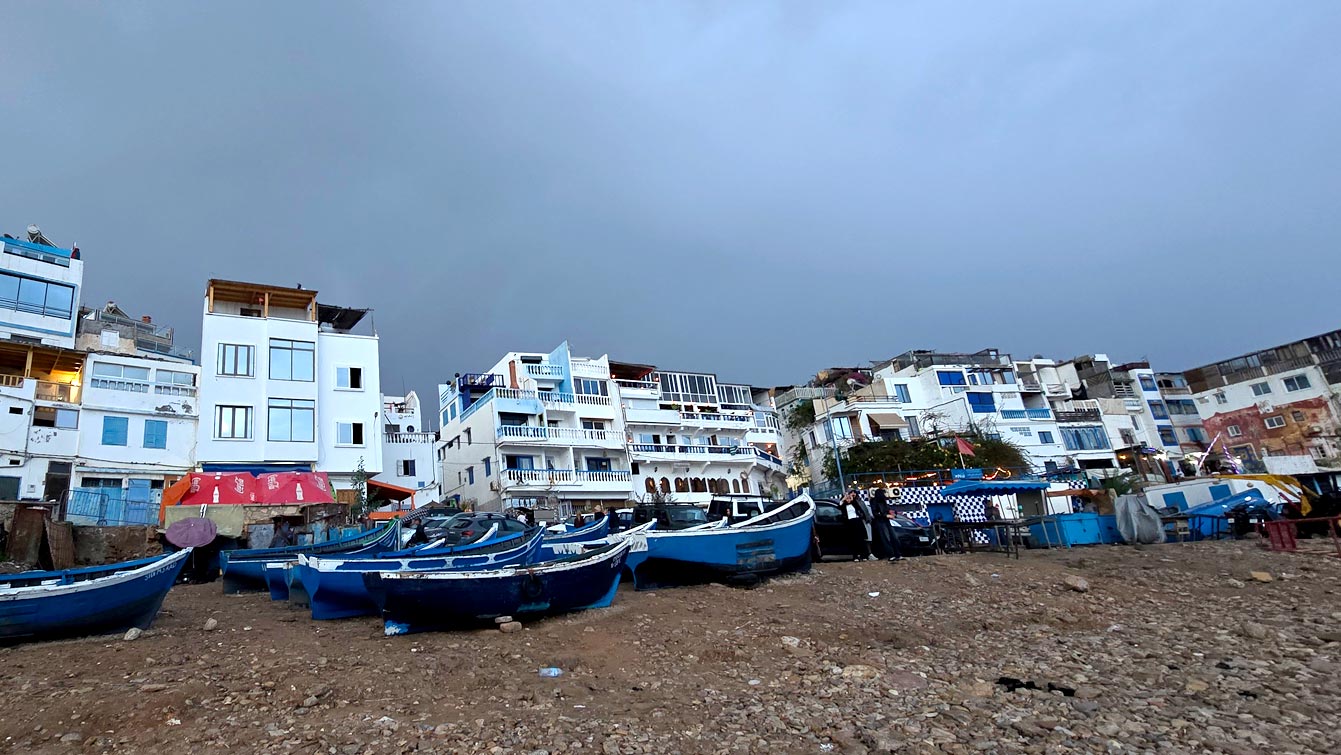 Barques bleues de Taghazout sur la plage à la tombée de la nuit devant les maisons blanches et bleues.