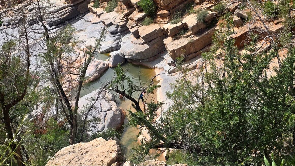 Vasque isolée vue depuis le sentier en hauteur, un baigneur assis sur la dalle Vallée du Paradis, Agadir