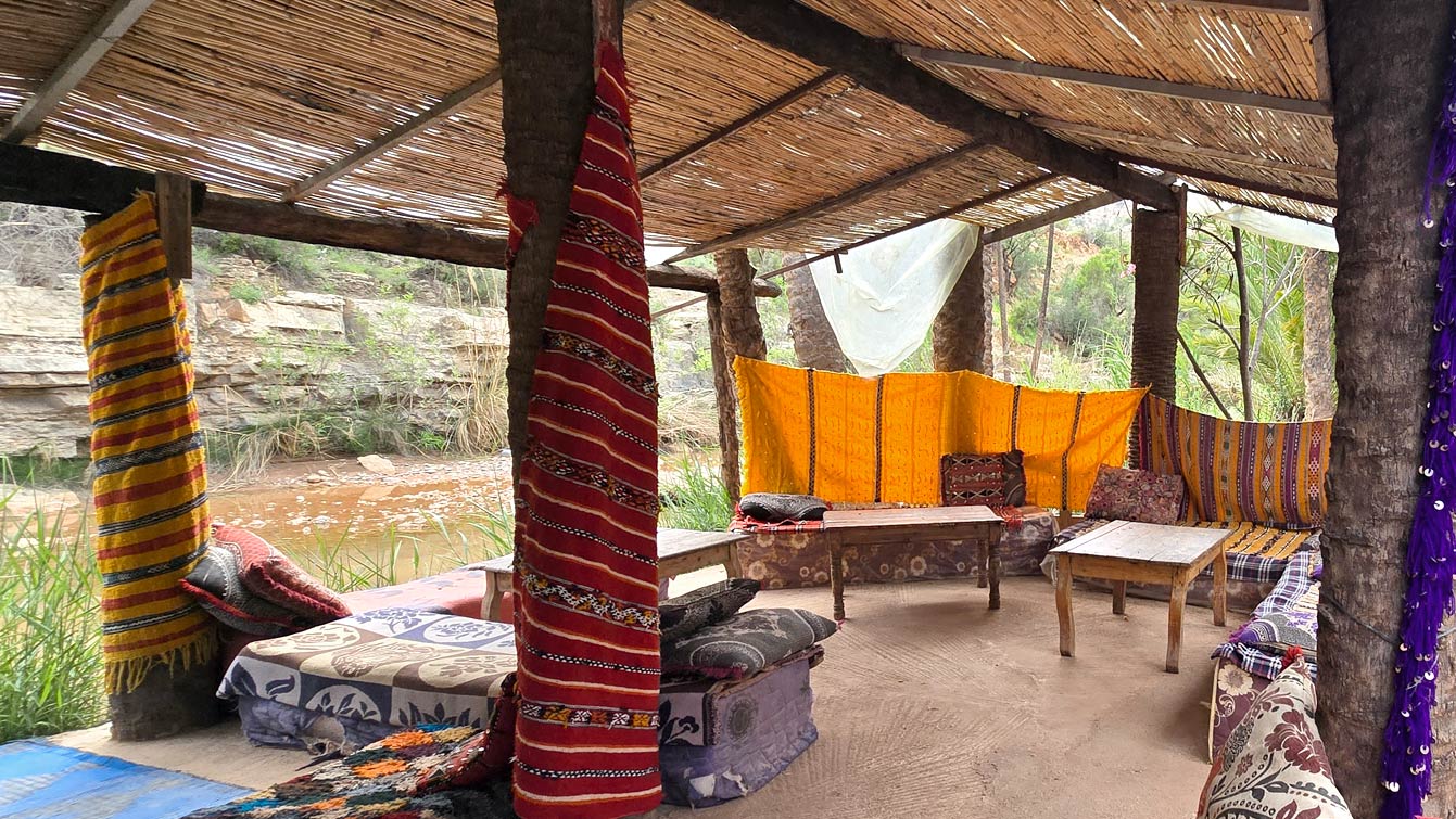 Salon berbère sous paillote avec tapis et coussins au bord de l'oued